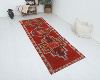 May include: A red, orange, and brown patterned runner rug with a geometric design. The rug has a fringed edge and is made of wool.