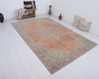 Puede incluir: Una alfombra rectangular grande con un intrincado diseño floral en tonos naranja, beige y morado. La alfombra tiene un aspecto descolorido, lo que sugiere que es vintage. La alfombra está colocada sobre un suelo blanco. Dimensiones: 200 cm x 300 cm.