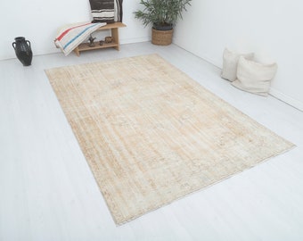 Può includere: Un grande tappeto rettangolare beige dall'aspetto vintage e usurato. Il tappeto ha un design sbiadito e fantasia ed è posto su un pavimento bianco. Cuscini decorativi e una panca in legno sullo sfondo.