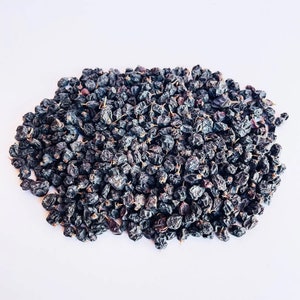 May include: A close-up of a pile of dried black currants. The currants are small and round, and they have a dark, almost black color.