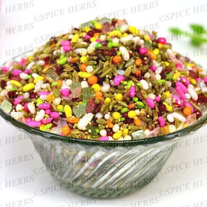May include: A clear glass bowl filled with a colorful mix of candy, seeds, and spices. The candy is in various colors, including pink, yellow, green, and red. The seeds are green and brown, and the spices are brown and black.