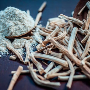 May include: A wooden spoon filled with white powder, surrounded by dried, light brown sticks on a dark brown surface.