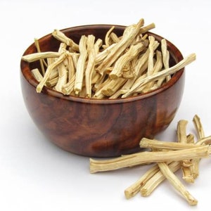 May include: A wooden bowl filled with dried, light brown, thin sticks. Some sticks are scattered on a white surface.