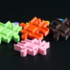 May include: Four colorful plastic puzzle pieces in green, orange, pink, and brown. The pieces are shaped like squares with rounded edges and have a grid pattern.