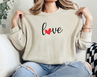 May include: A beige sweatshirt with the word "love" in black script with a red heart in the middle of the word.