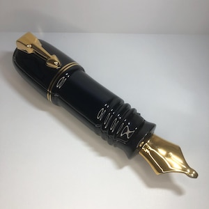 Può includere: Una penna stilografica nera con dettagli dorati. La penna ha un pennino dorato e una clip dorata. Il corpo della penna è nero lucido con finiture dorate. Uno strumento di scrittura classico.