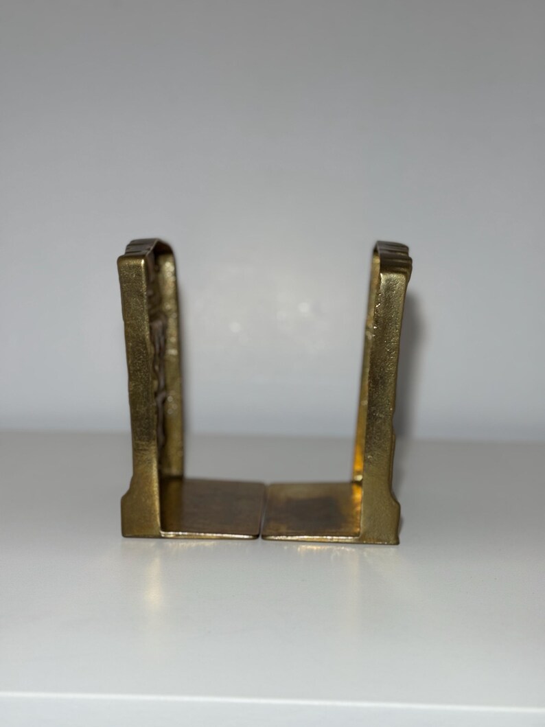 Puede incluir: Dos sujetalibros antiguos de lat&oacute;n. Cada sujetalibros tiene una base rectangular y una parte superior arqueada decorativa. El lat&oacute;n tiene un tono dorado c&aacute;lido, y el dise&ntilde;o parece vintage, agregando un toque de elegancia cl&aacute;sica a cualquier estanter&iacute;a.