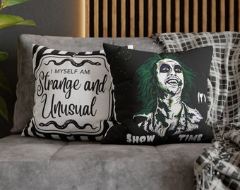 May include: Two decorative throw pillows on a gray couch. One pillow is black and white with the text "I MYSELF AM Strange and Unusual". The other pillow is black with a green and white graphic of a character and the text "SHOW TIME".
