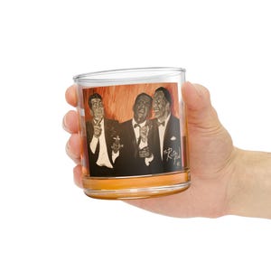 May include: A clear glass tumbler with a printed image of three men in black and white. The image is of the Rat Pack, a group of entertainers from the 1960s. The image is surrounded by a brown border.