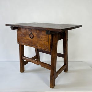 May include: A dark brown wooden side table featuring a rectangular top, a single drawer with a central circular metal pull, and four straight legs connected by lower horizontal stretchers with a scalloped edge detail on the front support.
