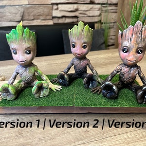 Puede incluir: Tres versiones diferentes de una pequeña maceta Groot verde, marrón y naranja. Cada maceta está sentada en una alfombra de hierba verde. El texto "Versión 1 | Versión 2 | Versión 3" está impreso debajo de las macetas.