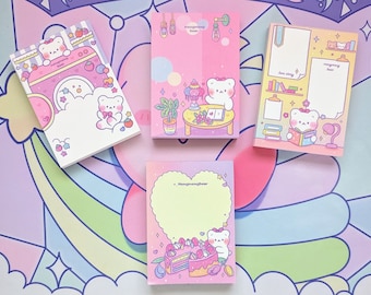 Puede incluir: Cuatro blocs de notas rosas y blancos con osos de dibujos animados y  ilustraciones. Los blocs de notas presentan diferentes diseños, incluyendo un oso en una nube, un oso leyendo un libro, un oso con un pastel y un oso con una lámpara. Los blocs de notas son perfectos para tomar notas, escribir recordatorios o dejar mensajes.