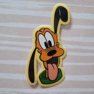 May include: A yellow sticker featuring a cartoon image of Pluto, a dog with orange fur, black ears, and a large, pink tongue sticking out. Pluto is wearing a green collar.