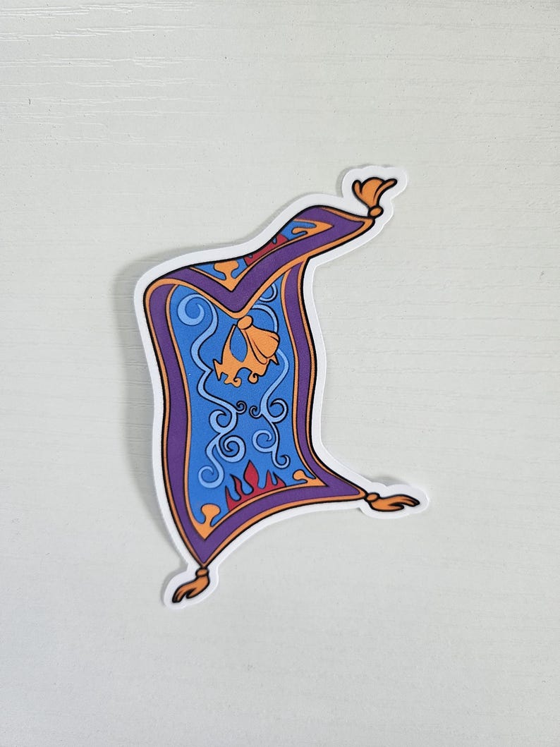 May include: A sticker featuring a stylized, cartoon-like image of a magic carpet. The carpet is primarily blue with purple borders and gold accents. The design includes swirls, a bell-shaped detail, and flame-like patterns.