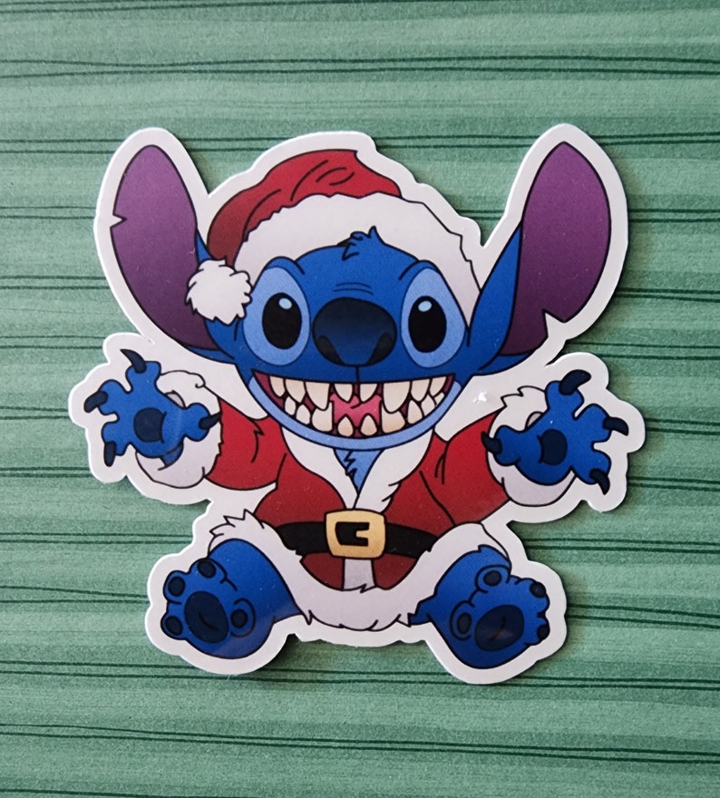 May include: A blue Stitch character wearing a red and white Santa Claus suit with a white fur trim. The character has a big grin and is holding out its arms.