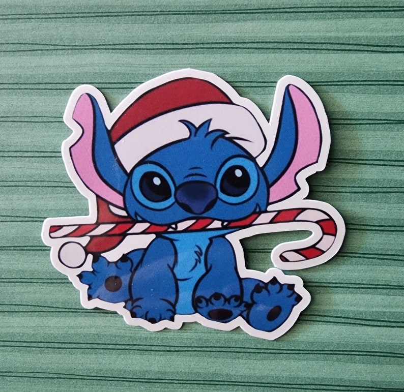 May include: A blue cartoon character wearing a red Santa hat and holding a candy cane. The character has large eyes and a wide smile.