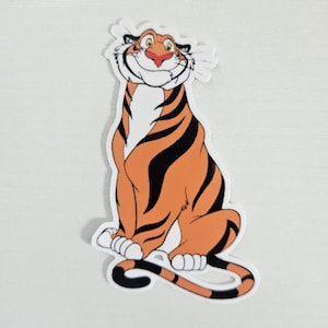 May include: A sticker featuring a cartoon tiger with orange fur and black stripes. The tiger is smiling with a red nose and white whiskers. The sticker is sitting down with its tail curled.