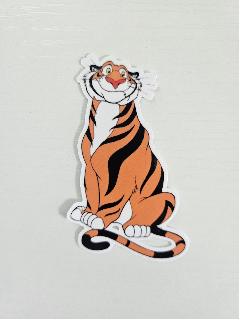May include: A sticker featuring a cartoon tiger with orange fur and black stripes. The tiger is smiling with a red nose and white whiskers. The sticker is sitting down with its tail curled.