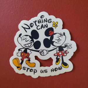 May include: A white sticker featuring Mickey and Minnie Mouse holding hands, with the text "Nothing Can Stop Us Now." Mickey is wearing red shorts and yellow shoes, while Minnie wears a red polka-dot skirt and a red bow. A yellow butterfly is also present.