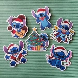 May include: Six blue Stitch character Christmas stickers with different poses and designs. The stickers feature Stitch wearing a Santa hat, holding a Christmas tree, and decorating with lights. The stickers are perfect for adding a touch of Disney magic to your holiday decor.