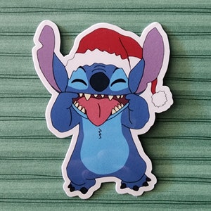 May include: A blue cartoon character with a red Santa hat, sticking out its tongue and making a silly face. The character has large ears and a wide smile.