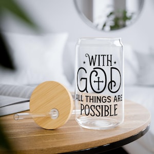Puede incluir: Un vaso transparente con forma de lata con tapa y pajita de bambú. El vaso presenta el texto negro "WITH GOD ALL THINGS ARE POSSIBLE". La tapa y la pajita están sobre una mesa de madera.