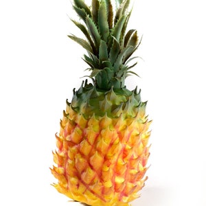 May include: A detailed artificial pineapple, showing a gradient of colours. The top has green leaves, while the body transitions from green to yellow and orange. The pineapple has a textured surface, and is set against a white background.