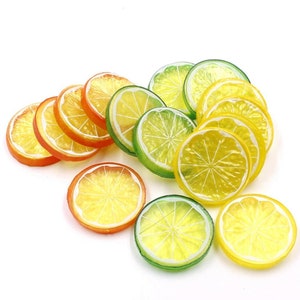 May include: A collection of artificial fruit slices, including orange, lemon, and lime, in various shades of yellow, green, and orange. The slices are arranged in a pile, with the lime slices on top.