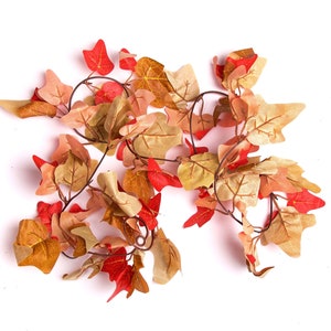 May include: A garland of artificial leaves in shades of red, brown, and beige. The leaves are arranged in a cascading pattern, creating a realistic and festive look.