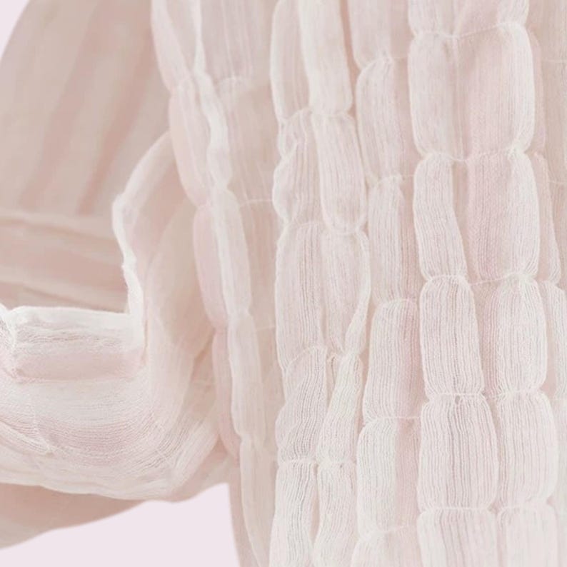 May include: A pale pink scarf featuring a textured, puckered fabric design. The material is lightweight and semi-sheer, displaying a series of vertical, gathered channels that create a repeating, soft, pillowed effect across the entire surface.