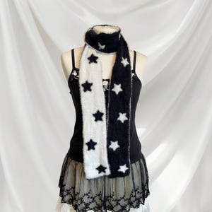 May include: A black and white fuzzy scarf with star patterns. The scarf is worn around the neck of a mannequin wearing a black tank top and a black lace skirt.