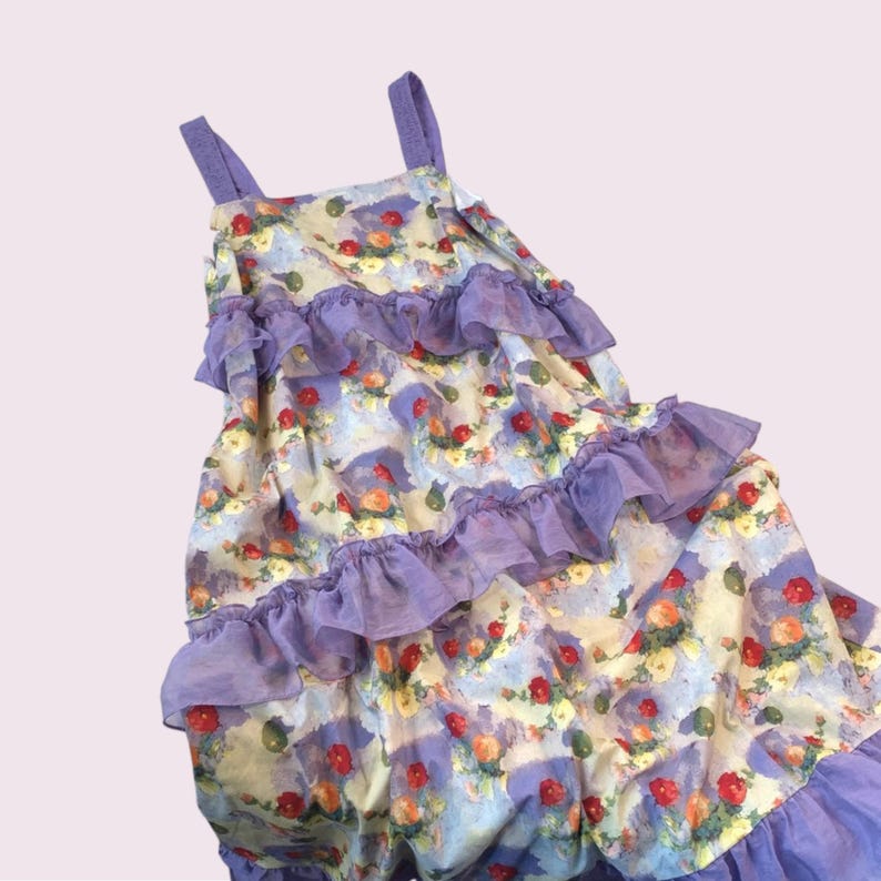May include: A sleeveless dress with a floral pattern in shades of red, yellow, and green on a light blue and cream background. The dress features layers of purple ruffles and straps.