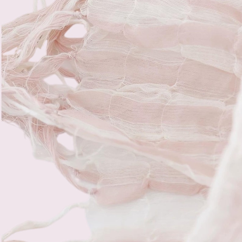May include: A sheer, lightweight fabric textile featuring a delicate grid-like weave pattern. The material displays alternating horizontal bands of soft, pale pink and crisp white, with loose, frayed thread ends visible along the left side edge.