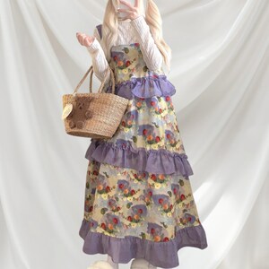 May include: A floral print dress with lavender ruffles and a straw tote bag. The dress features a watercolor-style pattern with red, yellow, and blue flowers. The tote bag has a bear-shaped embellishment.