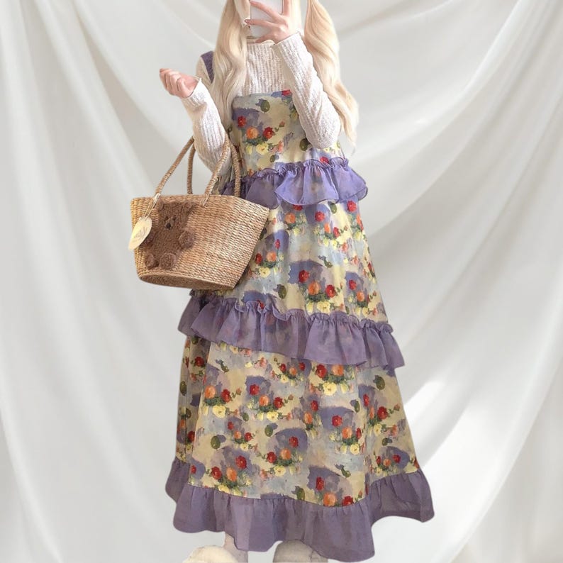 May include: A floral print dress with lavender ruffles and a straw tote bag. The dress features a watercolor-style pattern with red, yellow, and blue flowers. The tote bag has a bear-shaped embellishment.