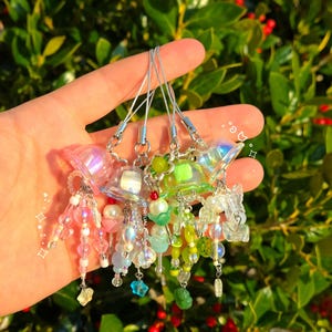 May include: A set of five iridescent and green charm bracelets with beaded charms. Each charm features a clear, dome-shaped top with a small, colorful bead inside. The charms are attached to silver chains with small silver beads.