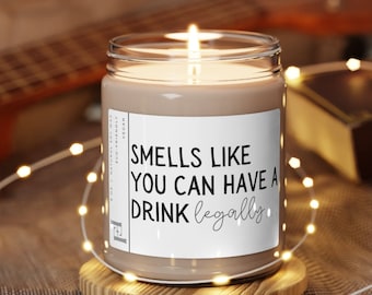 Op de afbeelding: Een bruine sojawas-kaars met een wit label waarop staat "Smells like you can have a drink legally". De kaars is aangestoken en staat op een houten onderzetter.