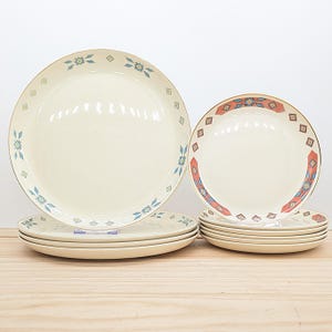 May include: A set of cream-colored ceramic plates with decorative geometric patterns in blue, orange, and gold. The plates include dinner plates and smaller plates, suitable for serving meals. The design features a border of repeating shapes.