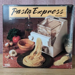 May include: A box for a Pasta Express pasta maker, Model X2000, with the machine extruding fresh pasta. The box features images of ingredients like tomatoes, eggs, and garlic. Includes instructional videotape.