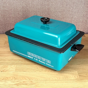Könnte beinhalten: Ein türkisfarbener NESCO 4 Qt. Bräter mit schwarzem Griff und Knauf. Der rechteckige Ofen hat eine schwarze Verkleidung und ein weißes Etikett mit Kochanweisungen. Der Ofen steht auf einer Holzoberfläche.