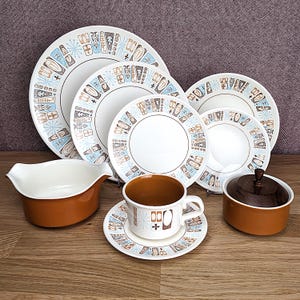 Könnte beinhalten: Ein Vintage-Geschirr-Set im Mid-Century-Modern-Stil mit weißen Tellern mit einem geometrischen Muster in Blau, Braun und Beige. Das Set umfasst Teller, Schalen, eine Sauciere, eine Tasse mit Untertasse und eine Schüssel mit Deckel.