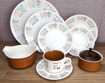 May include: A vintage mid-century modern dinnerware set featuring white plates with a blue, brown, and tan geometric pattern. The set includes plates, bowls, a gravy boat, a cup and saucer, and a covered dish.