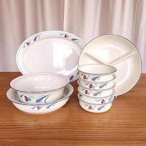 Può includere: Un set di piatti in ceramica bianca con un motivo floreale blu e verde. Il set comprende un grande piatto ovale, un piatto da portata diviso e sei ciotole.