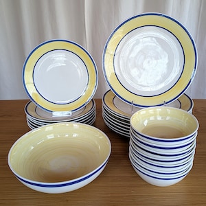 Puede incluir: Un juego de vajilla de cerámica a rayas amarillas y azules. El juego incluye platos, cuencos y una fuente para servir.