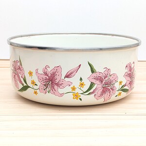May include: White enamel bowl with a floral design featuring pink lilies and yellow flowers. The bowl has a silver rim.