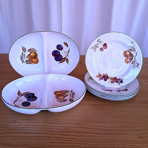 Puede incluir: Dos platos de servir divididos con un borde verde y un diseño de pera y cereza. Una pila de cinco platos blancos con un borde verde y un diseño de pera, cereza y mora.