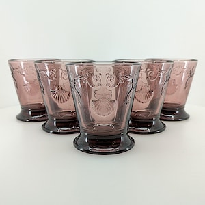 Könnte beinhalten: Satz mit sechs violetten Gläsern mit einem geprägten Muschel-Design. Die Gläser haben einen ausgestellten Boden und eine breite Öffnung.