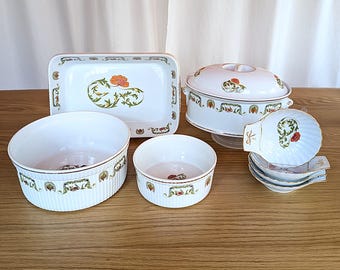 May include: A set of white ceramic baking dishes with a floral design. The set includes a large oval casserole dish with a lid, a rectangular baking dish, two small round bowls, and three small shell-shaped dishes.