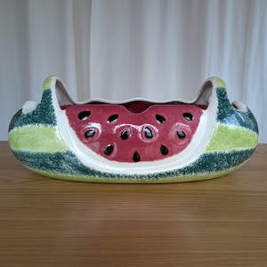 Könnte beinhalten: Eine Keramik-Servierschale in Wassermelonenform mit grünen und weißen Streifen und einer roten Wassermelonen-Scheibe im Inneren. Die Schale hat eine glänzende Oberfläche und ist perfekt zum Servieren von Obst oder Snacks.