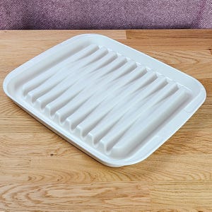 Peut inclure: Un plateau rectangulaire en plastique blanc doté d'une série de nervures parallèles en relief sur toute la surface. Le plateau présente des coins arrondis et une finition lisse et brillante, avec un motif rainuré fonctionnel pour le drainage.